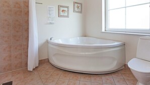 Une salle de bain équipée d’une baignoire, de toilettes et d’une fenêtre laissant entrer la lumière naturelle.