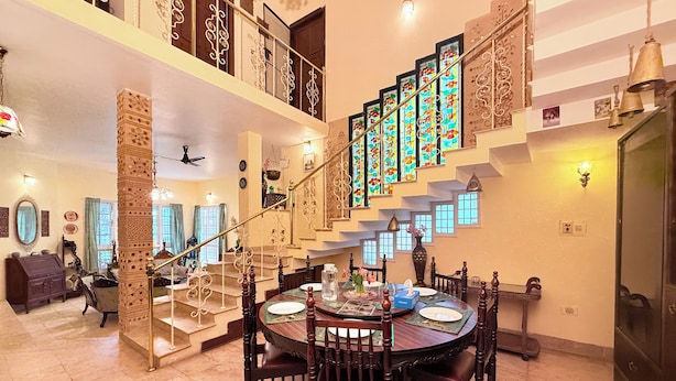 A spacious dining area with a high ceiling, ornate staircase, and a view of the upper floor. - Heritage Haven Luxury Spacez Villa (Bengaluru)