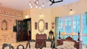 A traditional room with ornate furniture, a large mirror, and a view through a window with a grid pattern. - Heritage Haven Luxury Spacez Villa (Bengaluru)