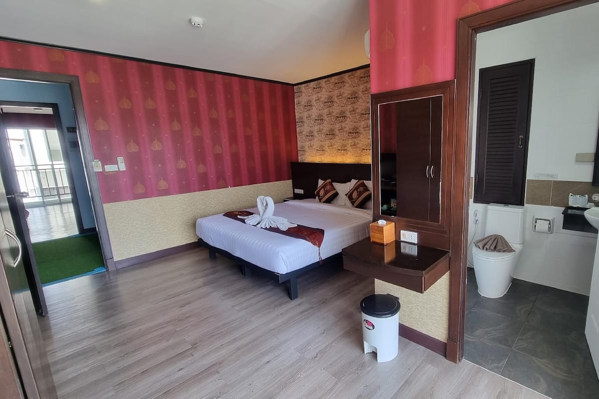 Une chambre d’hôtel avec un lit, un petit tabouret, un miroir, un lavabo et des toilettes.