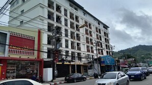 Ein mehrstöckiges Gebäude mit Balkonen, einer roten Fassade und parkenden Autos vor der Straße.