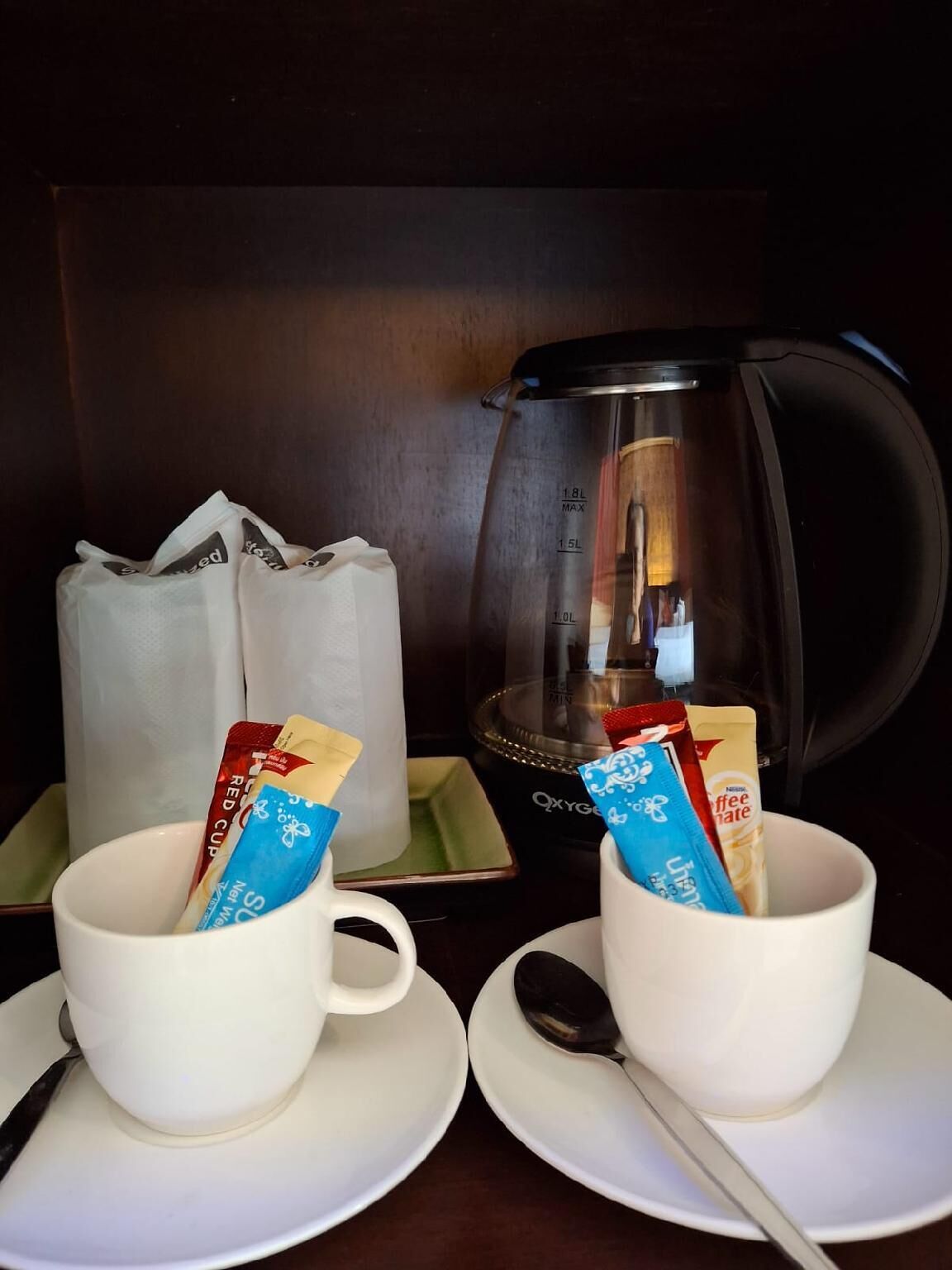 Un angolo caffetteria con due tazze, un bollitore e confezioni di caffè e panna.