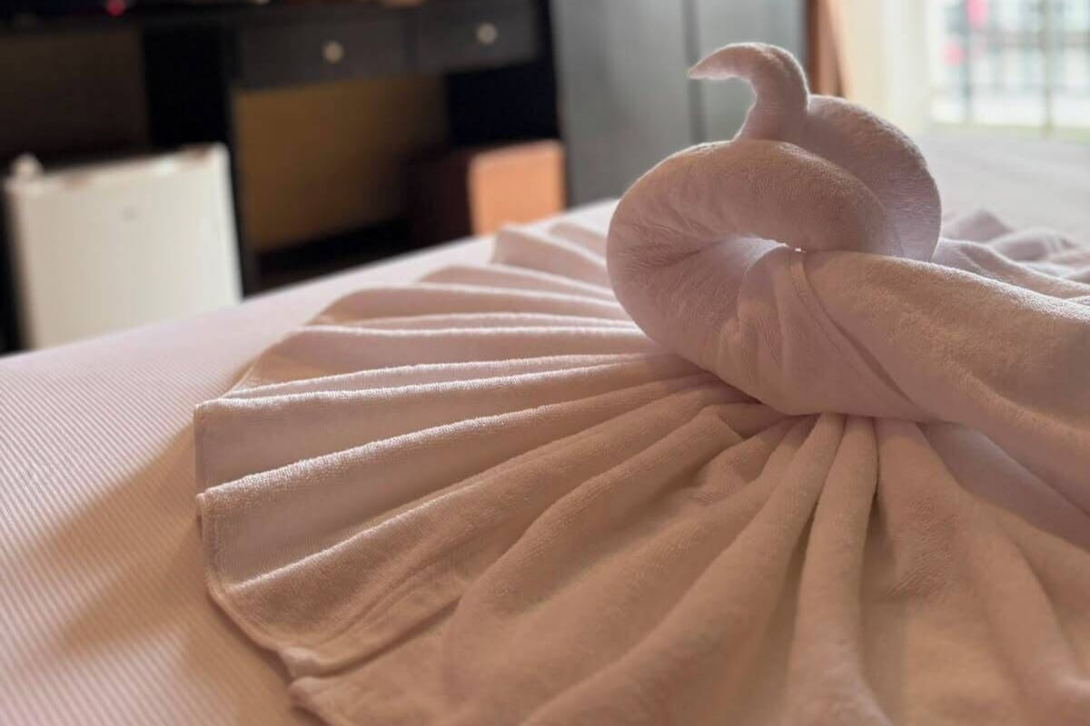 Una cama bien hecha con una toalla doblada en forma de lazo.