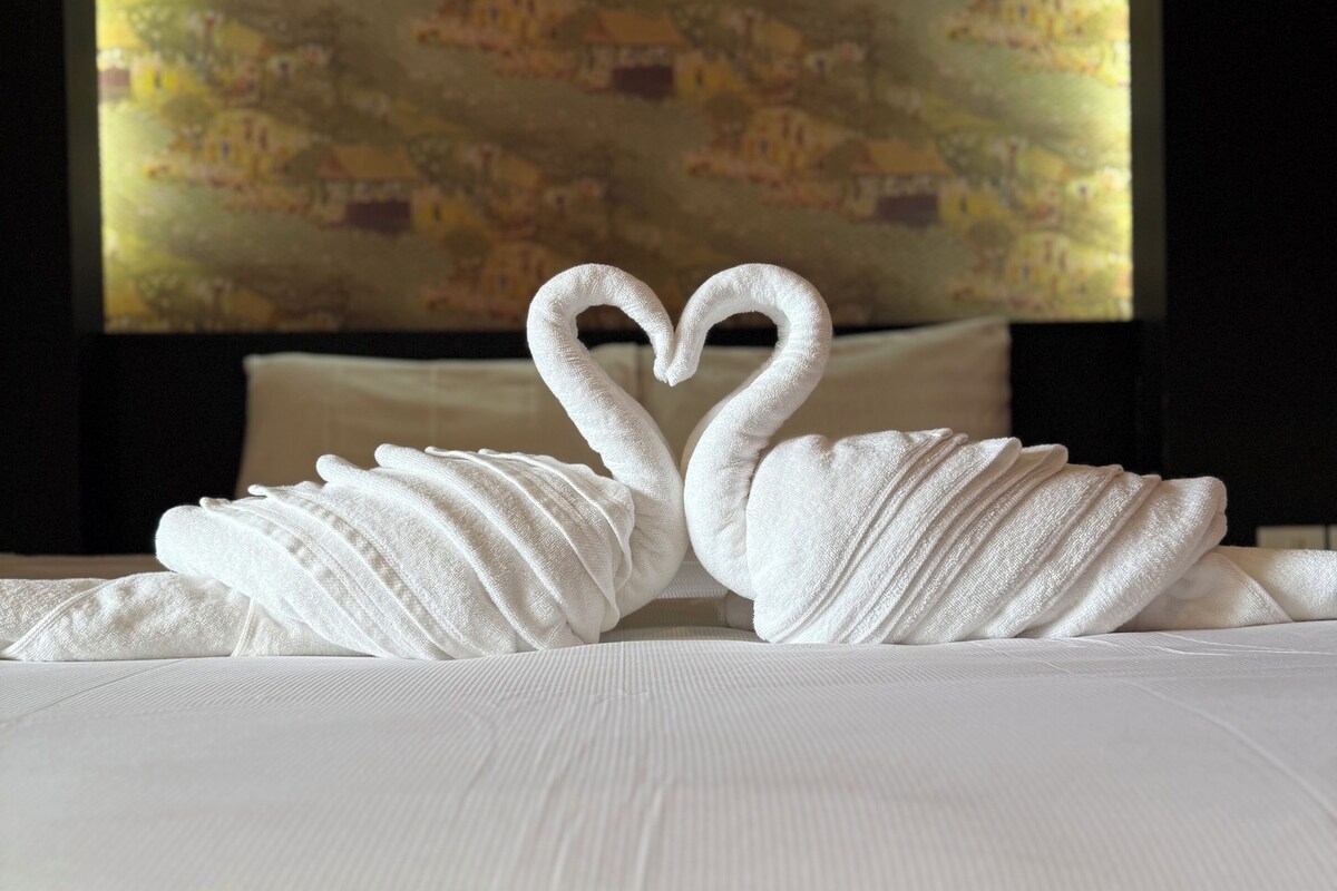 Una cama con una colcha blanca y dos toallas dispuestas en forma de cisnes.