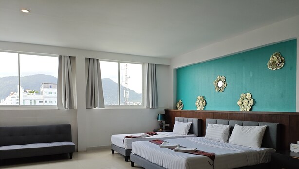 Ein Hotelzimmer mit zwei Betten, einem Sofa und einem großen Fenster mit Blick auf Gebäude und Berge.
