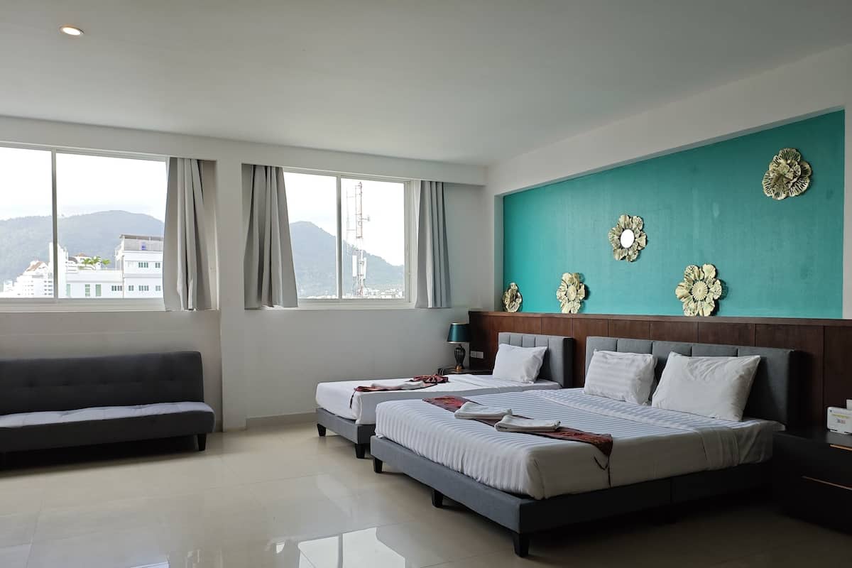 Une chambre d’hôtel avec deux lits, un canapé et une grande fenêtre donnant sur des immeubles et des montagnes.