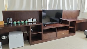 Ein Hotelzimmer mit Holzschreibtisch, Flachbildfernseher, Minikühlschrank und einer Kaffeestation.
