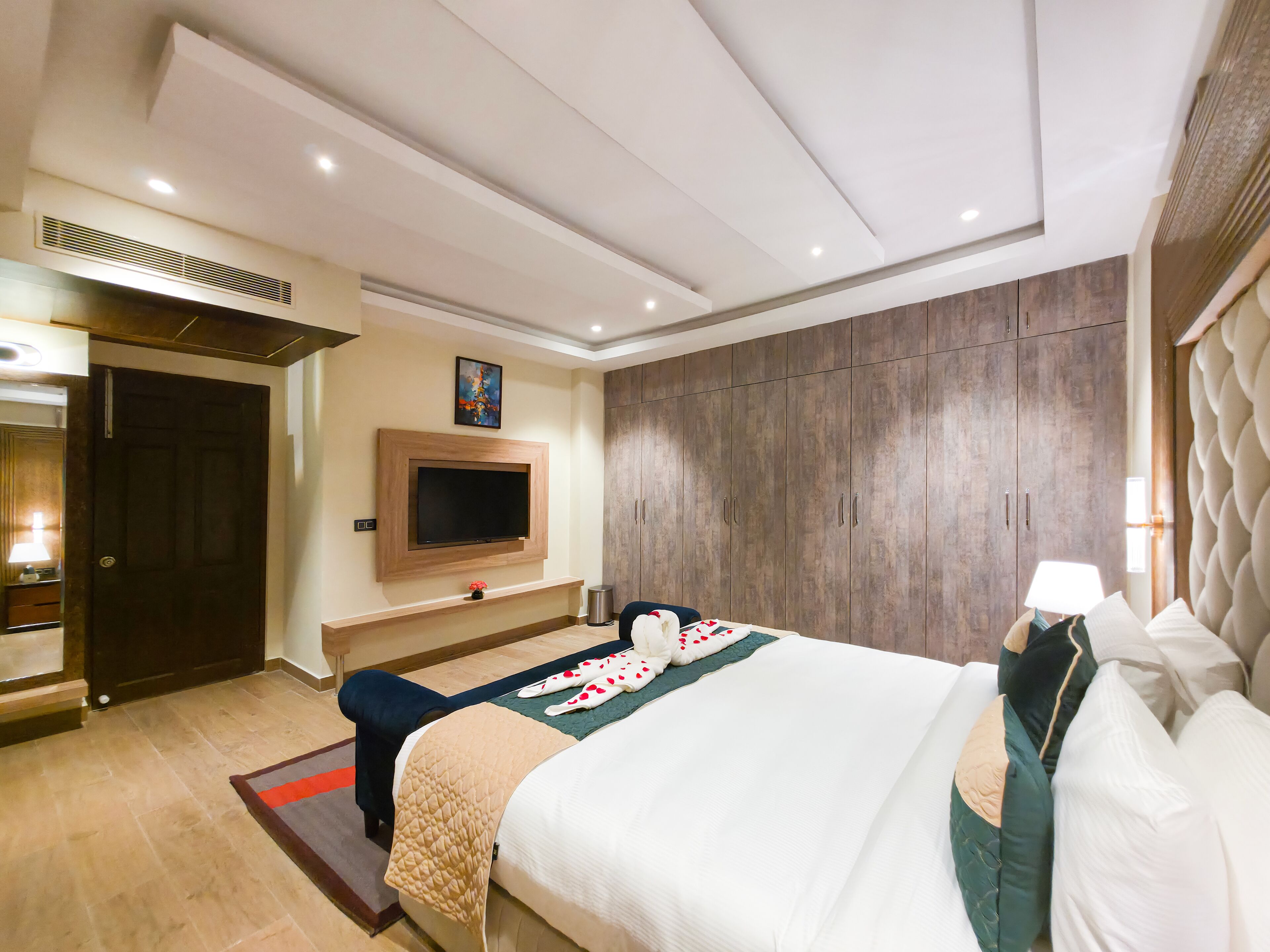 A hotel room with a large bed, a TV mounted on the wall, a wooden wardrobe, and a mirror.