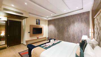 A hotel room with a large bed, a TV mounted on the wall, a wooden wardrobe, and a mirror.
