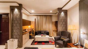 A modern living room with a sofa, armchair, coffee table, and a small kitchen area with a lamp.