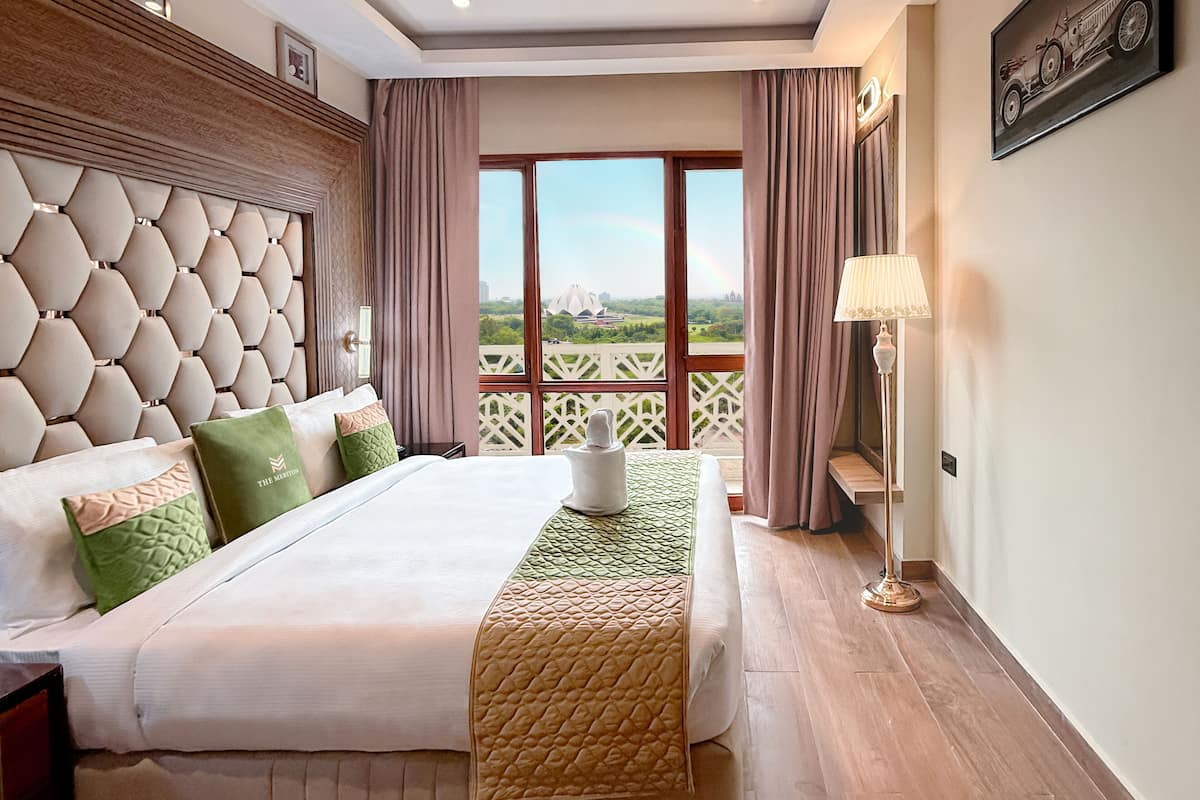Ein Hotelzimmer mit einem großen Bett, Blick auf eine Stadtansicht und einem Balkon mit Geländer.