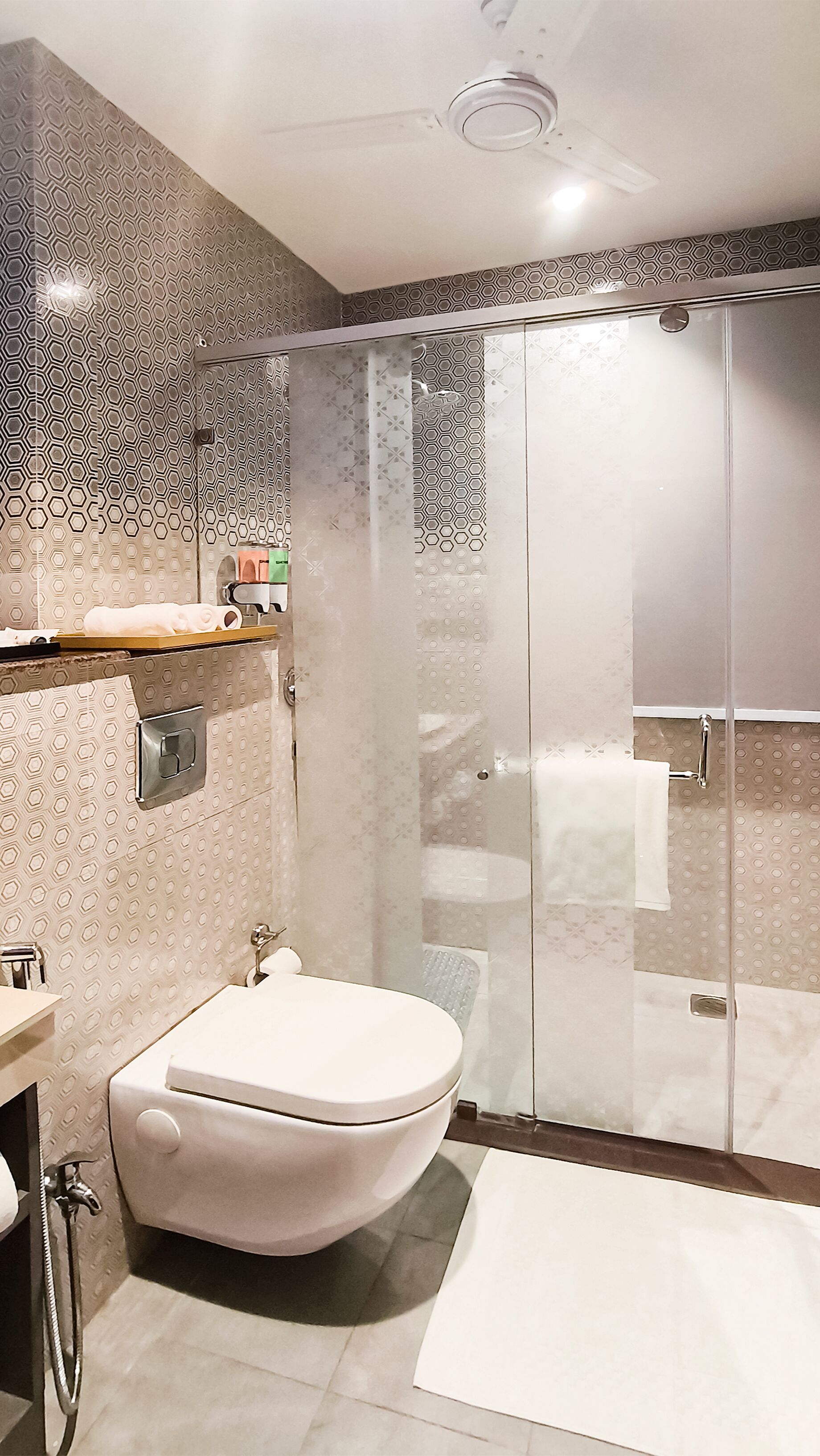 A modern bathroom with a freestanding toilet, a glass-enclosed shower, and a patterned wall design.