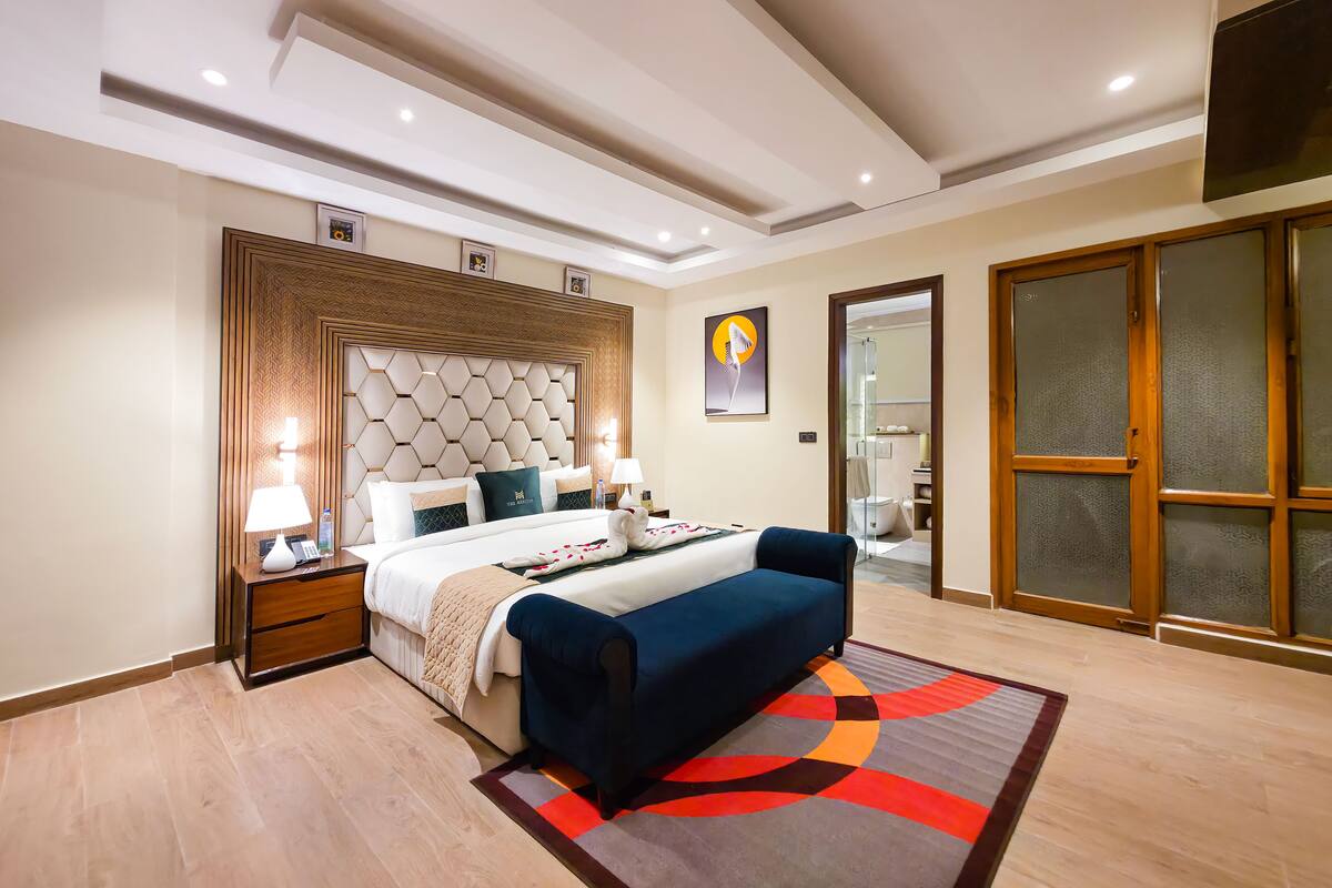 Ein modernes Hotelzimmer mit einem großen Bett, einem Nachttisch mit Lampe, einem blauen Sofa und einem farbenfrohen Teppich.