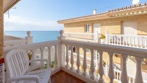 A balcony with white railings overlooking a beach and a building with a tiled roof. - El Morche - Apartment In El Morche. Free Wifi (El Morche, Málaga)