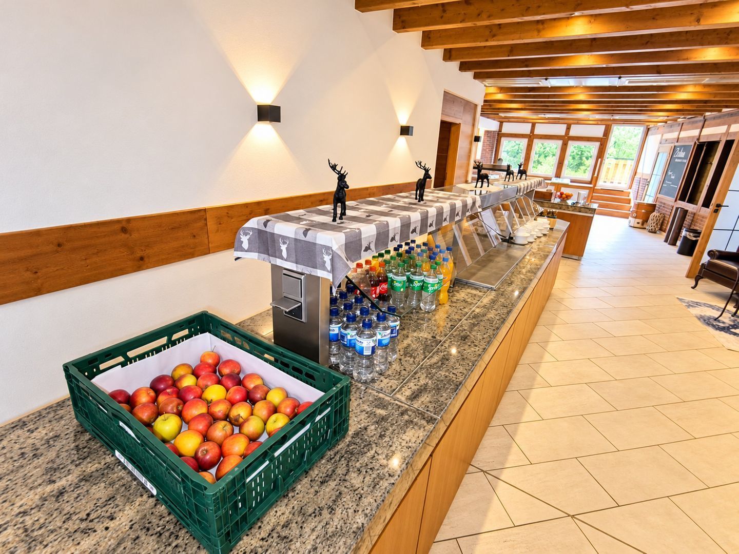 Zona de bufé con una exhibición de frutas, dispensadores de bebidas y una larga barra.