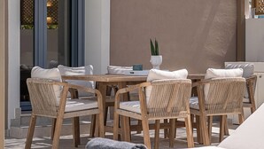 An outdoor seating area with a table and chairs, a potted plant, and a view of the interior through a glass door. - Villa Seyian-Charming 3 bedroom villa-Private Pool (CHANIA)