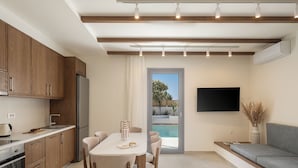 A modern kitchen with wooden cabinets, a dining table with chairs, a built-in oven, and a TV mounted on the wall. - Villa Seyian-Charming 3 bedroom villa-Private Pool (CHANIA)
