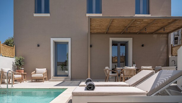A modern building with a pool area, including lounge chairs and a table with chairs. - Villa Seyian-Charming 3 bedroom villa-Private Pool (CHANIA)