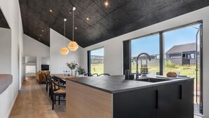 Une cuisine moderne dotée d’un grand îlot central, de meubles noirs et offrant une vue sur l’extérieur.