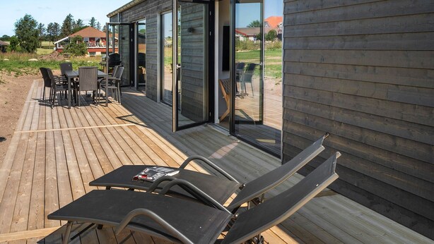 Une terrasse extérieure avec une table et des chaises, un fauteuil de relaxation et une porte-fenêtre coulissante donnant sur un espace patio.