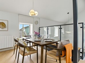 A modern dining area with a wooden table, chairs, and a hanging light fixture.