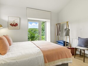 A bedroom with a bed, a window, a hanging chair, and a view of greenery outside.