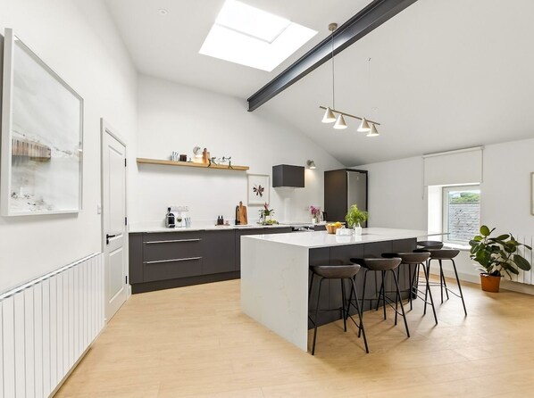 A modern kitchen with a central island, bar stools, and a skylight.