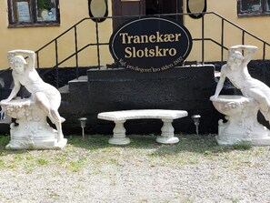 A building entrance with a sign reading "Traneaker Slotskro" and two statues on either side of a bench. - 2 Person Holiday Park Home in Tranekaer (Tranekaer)