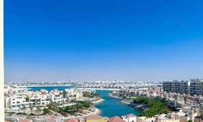 A coastal cityscape with a river, modern buildings, and a clear blue sky. - Peaceful Lagoon View l 1BR in RAK With Balcony (Ras Al Khaimah)