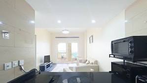 A modern living room with a flat-screen TV, a sofa, and a coffee table. There is a balcony with a view of the outside. - Peaceful Lagoon View l 1BR in RAK With Balcony (Ras Al Khaimah)