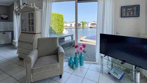 A room with a view of a canal, a chair, a TV, and a table with vases. - 2 bedroom lovely home in Lemmer (Lemmer)
