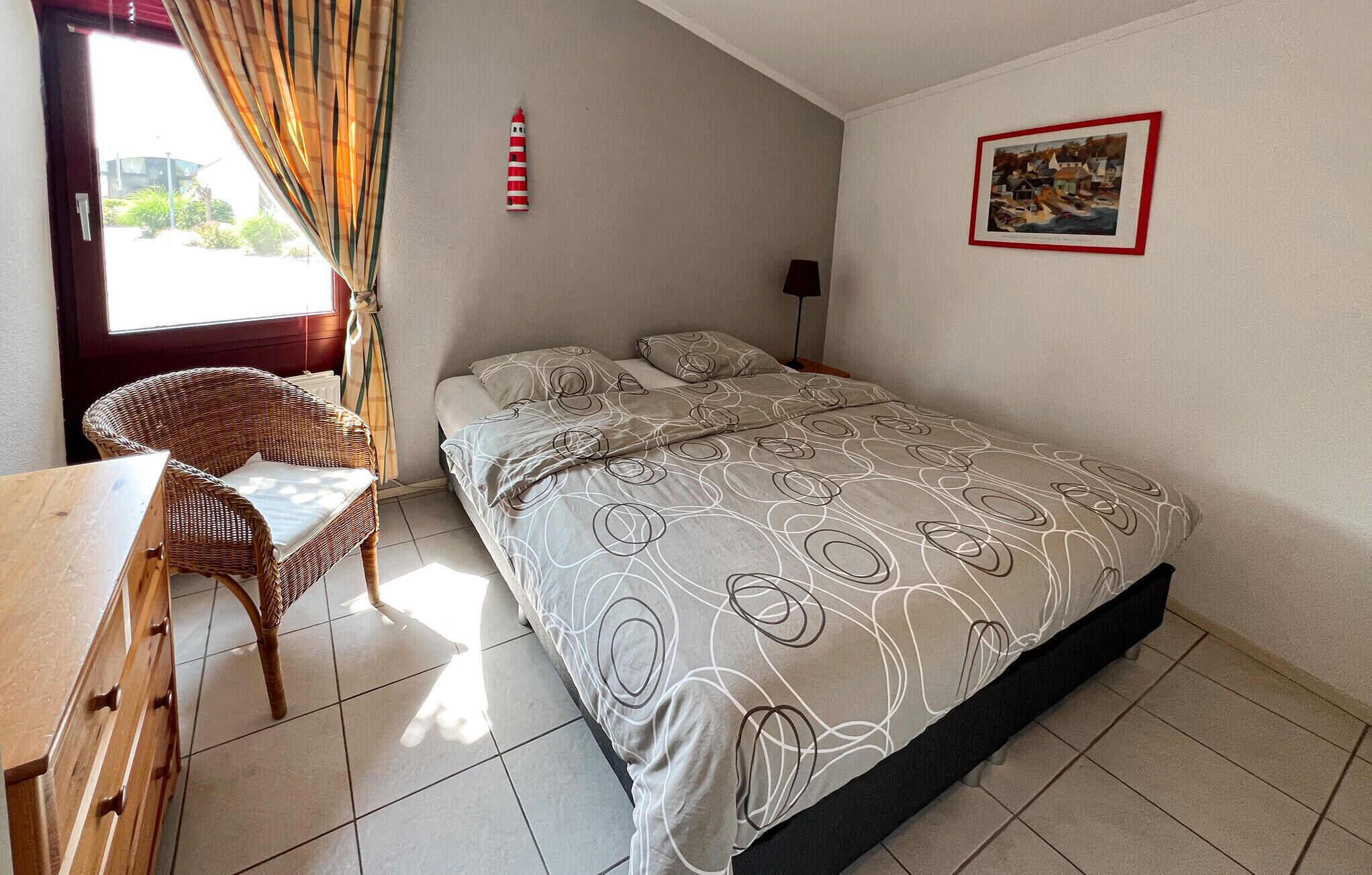 A bedroom with a bed, a chair, a table, a lamp, and a painting on the wall.
