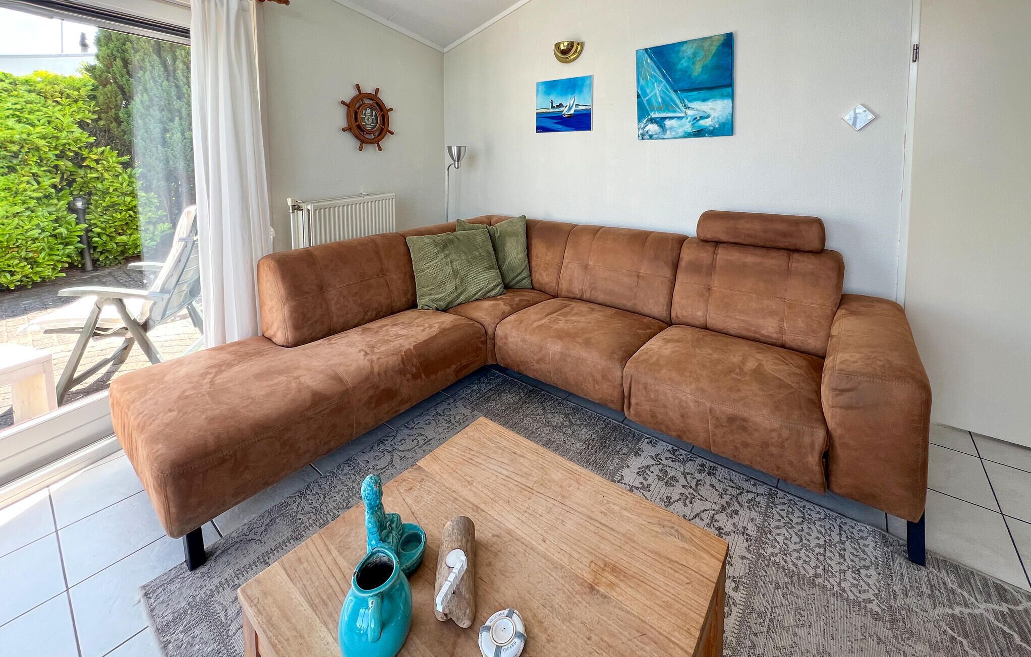 Una sala de estar moderna con un sofá seccional marrón, una mesa de centro de madera y vistas al exterior con follaje.