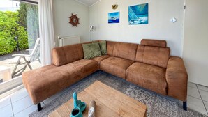 A modern living room with a brown sectional sofa, a wooden coffee table, and a view of greenery outside. - 2 bedroom lovely home in Lemmer (Lemmer)