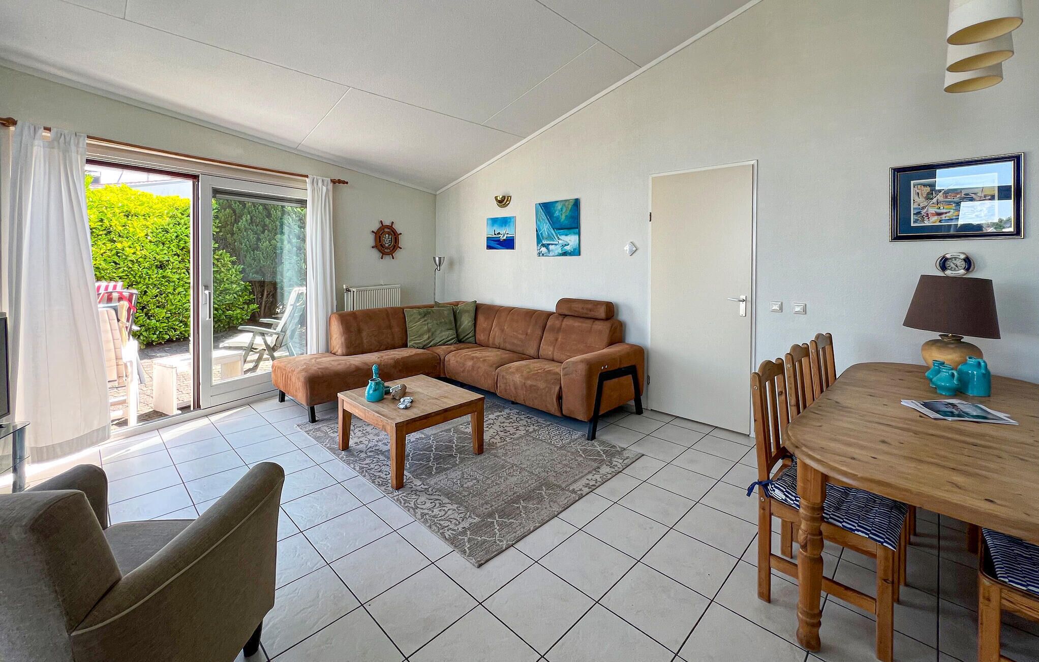 A living room with a sofa, a coffee table, and a dining table with chairs. There is a sliding glass door leading to an outdoor area with a table and chairs.