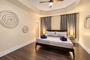 A bedroom with a bed, wooden floor, ceiling fan, and two wall-mounted lamps.