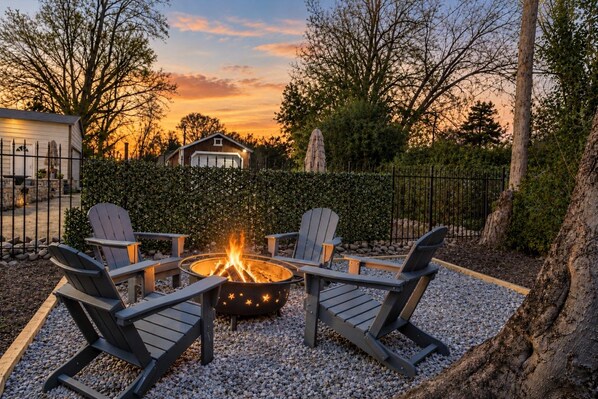 A patio with Adirondack chairs and a fire pit surrounded by gravel.