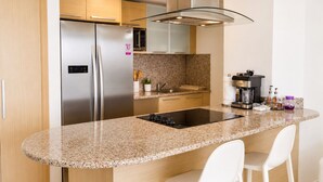 Una cocina moderna con encimera de granito, electrodomésticos de acero inoxidable y taburetes de bar blancos.
