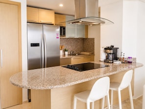 Una cocina moderna con encimera de granito, electrodomésticos de acero inoxidable y taburetes de bar blancos.