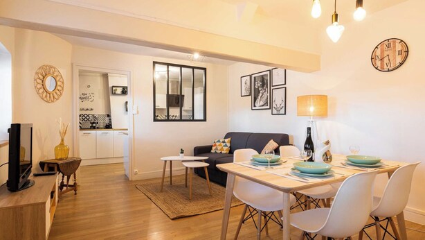 Un soggiorno moderno con zona pranzo, pavimento in legno e cucina visibile attraverso una porta aperta.