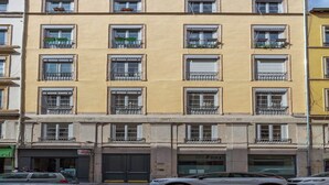 Un edificio de varios pisos con balcones, un escaparate visible y coches aparcados.
