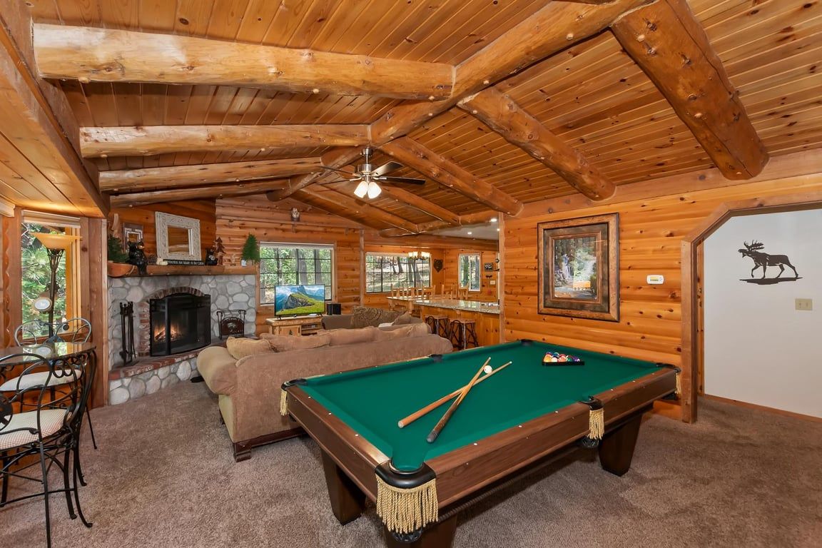 A cozy log cabin interior with a pool table, fireplace, and rustic decor.