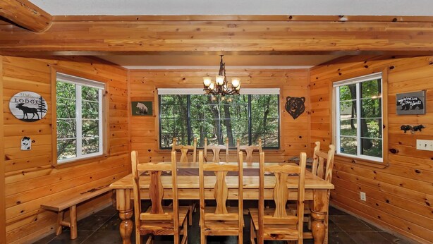 Comedor de cabaña de madera con una mesa grande y sillas, ventanas amplias con vistas al bosque y decoración temática de osos.