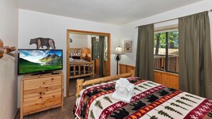 Un dormitorio con una cama, un tocador de madera, un televisor, un espejo y una ventana con cortinas.