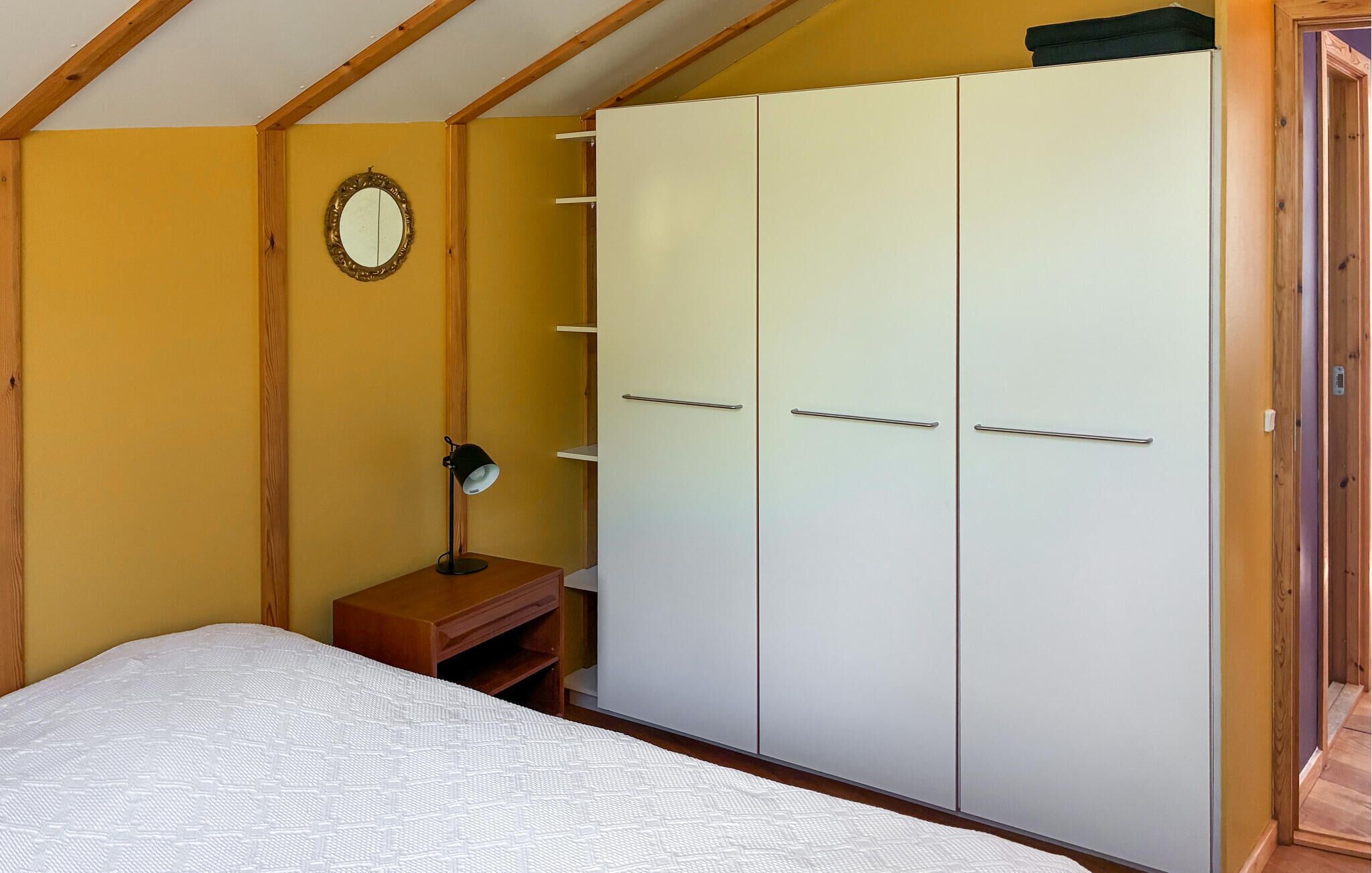 A bedroom with a bed, a wardrobe, a bedside table with a lamp, and a mirror on the wall.