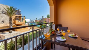 Un balcon avec une table préparée pour le petit-déjeuner, comprenant des fruits, du pain et du jus d’orange.