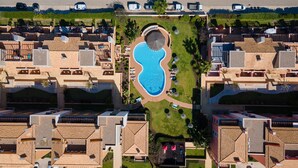 Vue aérienne d’un complexe hôtelier doté d’une piscine centrale, de plusieurs villas aux toits en tuiles et de pelouses bien entretenues.