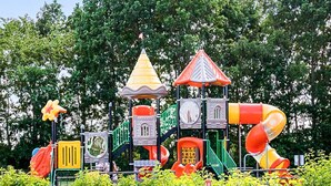 Een speeltuin met diverse speeltoestellen, waaronder glijbanen, klimgelegenheden en een klein torentje.