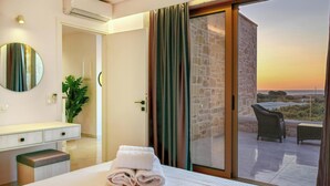 A hotel room with a bed, a bedside table, a mirror, a potted plant, and a view of the outdoors through a sliding glass door. - Koukis Villa With Sea View (Kissamos)