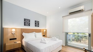 A modern hotel room with a large bed, wooden headboard, bedside lamps, a nightstand, and a view of the outdoors through a large window.